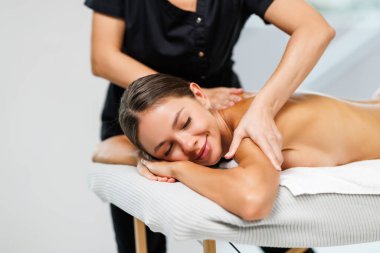 Genç bir kadın kaplıca salonundaki koltukta masaj yaptırıyor.