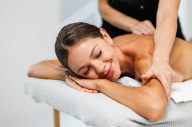 Genç bir kadın kaplıca salonundaki koltukta masaj yaptırıyor.