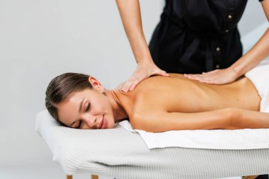 Genç ve rahat bir bayan, kaplıca salonundaki masözün omuzlarını ve sırtını ovaladığı masözle vücut masajından zevk alır.