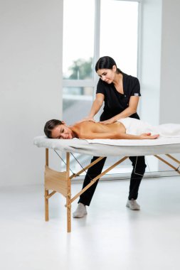 Genç ve rahat bir bayan, kaplıca salonundaki masözün omuzlarını ve sırtını ovaladığı masözle vücut masajından zevk alır.