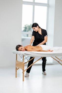 Genç ve rahat bir bayan, kaplıca salonundaki masözün omuzlarını ve sırtını ovaladığı masözle vücut masajından zevk alır.