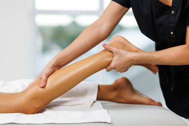 Masaj terapistinin elleri masaj salonundaki genç bayanın bacaklarına masaj yapıyor.