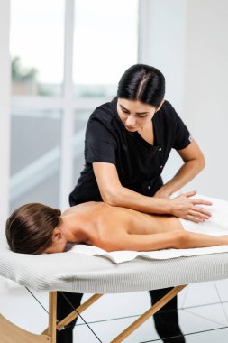 Masaj terapisti sırtına masaj yaparken rahat bir kadın masaj masasında yatıyor.