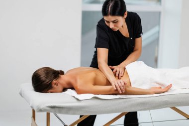 Masaj terapisti sırtına masaj yaparken rahat bir kadın masaj masasında yatıyor.