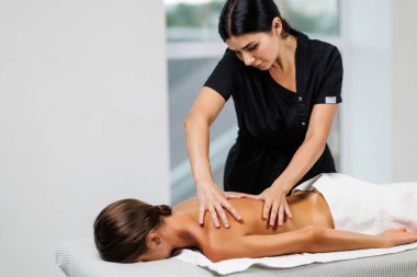 Masaj terapisti sırtına masaj yaparken rahat bir kadın masaj masasında yatıyor.