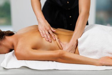 Masaj terapisti sırtına masaj yaparken rahat bir kadın masaj masasında yatıyor.