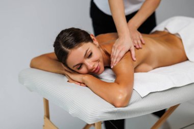 Profesyonel masaj terapisti, masaj masasında uzanan tanınmayan genç bir kadının sırtına masaj yapıyor. Mükemmel ciltli güzel çıplak kız rahatlatıcı bir masaj yaptırıyor. Vücut bakımı kavramı.