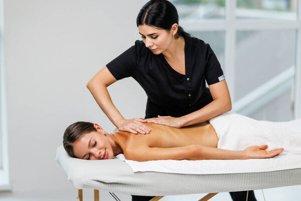 Body massage treatment. Woman having massage in the spa salon. Masseur working on his back.