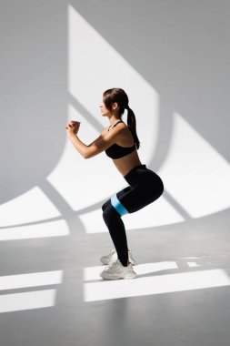 Beyaz arka planda direniş bandı döngüsüyle bodur egzersizleri yapan sportif bir kadın. Spor konsepti