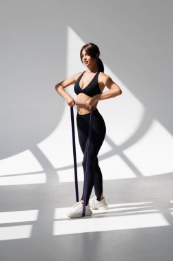 Beyaz arka planda izole edilmiş bir direniş bandıyla spor giyinen genç bir kadının tam boy profil çekimi.