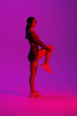 Mor ışıklı arka planda bacaklarını açan genç ve güzel bir kadın.