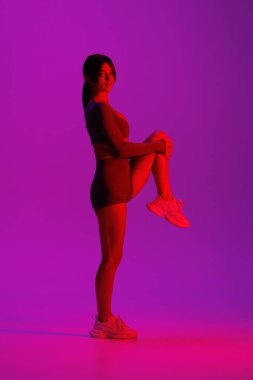 Mor ışıklı arka planda bacaklarını açan genç ve güzel bir kadın.