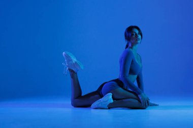 Yoga hocası, ya da binicilik pozu veren bir yoga hocası, stüdyoda mavi ve mor neon ışıklı bir yoga minderinde, düşük hamlenin bir çeşidi.