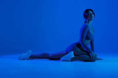 Yoga hocası, ya da binicilik pozu veren bir yoga hocası, stüdyoda mavi ve mor neon ışıklı bir yoga minderinde, düşük hamlenin bir çeşidi.