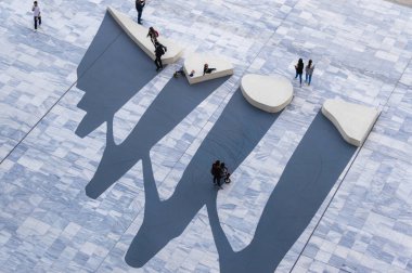 Yunanistan 'ın başkenti Atina' daki Stavros Niarchos Park 'ta, insanların yürüdüğü ve çocukların oynadığı mermer plazaya heykel bankları ile soyut sanat kurulumu dramatik gölgeler bırakıyor..