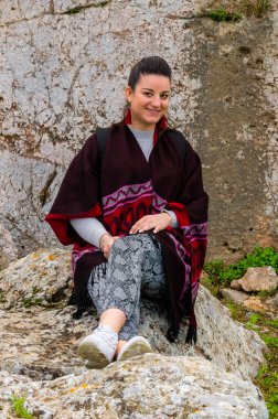 Atina, Yunanistan 'daki tarihi Pnyka tepesinde kayanın üzerinde oturan sırt çantası ve kırmızı pançolu bir kadının portresi.