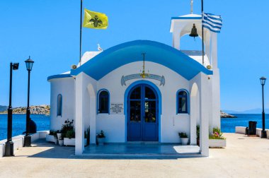 Yunanistan 'ın Megara kentindeki Pachi limanında bulunan Bakire Meryem' in Doğumu Şapeli 'nin beyaz ve mavi şapeli, çan kulesi, Yunan ve Bizans bayrakları ve yaz sahili manzaralı..
