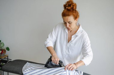 Genç bir kadın evde ütü masasını temiz ütülemek için kullanıyor..