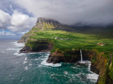 Dramatik Mulafossur şelalesi Gasadalur köyü ve arka planda kayalıklarla okyanusa dökülüyor..