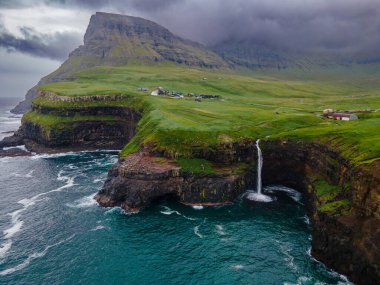 Dramatik Mulafossur şelalesi Gasadalur köyü ve arka planda kayalıklarla okyanusa dökülüyor..