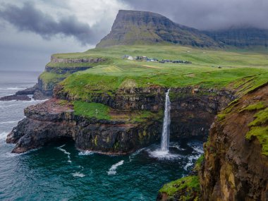 Dramatik Mulafossur şelalesi Gasadalur köyü ve arka planda kayalıklarla okyanusa dökülüyor..
