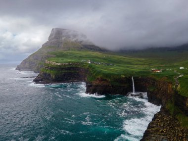 Dramatik Mulafossur şelalesi Gasadalur köyü ve arka planda kayalıklarla okyanusa dökülüyor..