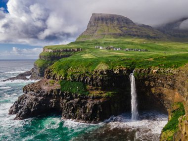 Dramatik Mulafossur şelalesi Gasadalur köyü ve arka planda kayalıklarla okyanusa dökülüyor..