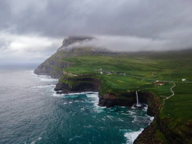 Dramatik Mulafossur şelalesi Gasadalur köyü ve arka planda kayalıklarla okyanusa dökülüyor..