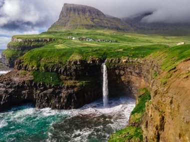 Dramatik Mulafossur şelalesi Gasadalur köyü ve arka planda kayalıklarla okyanusa dökülüyor..