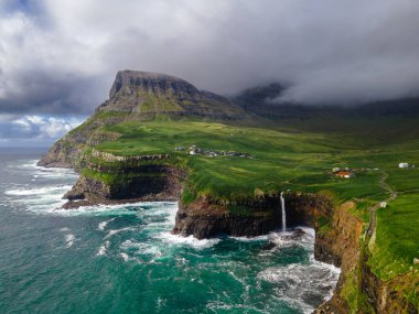 Dramatik Mulafossur şelalesi Gasadalur köyü ve arka planda kayalıklarla okyanusa dökülüyor..