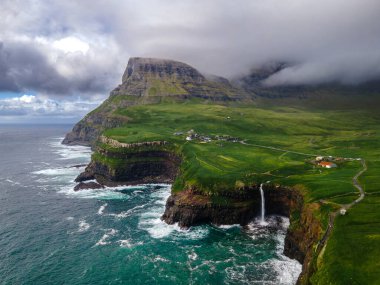 Dramatik Mulafossur şelalesi Gasadalur köyü ve arka planda kayalıklarla okyanusa dökülüyor..