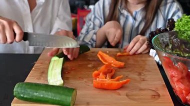 Anne ve genç kız şık, siyah bir mutfakta taze, sağlıklı bir salata hazırlıyorlar..