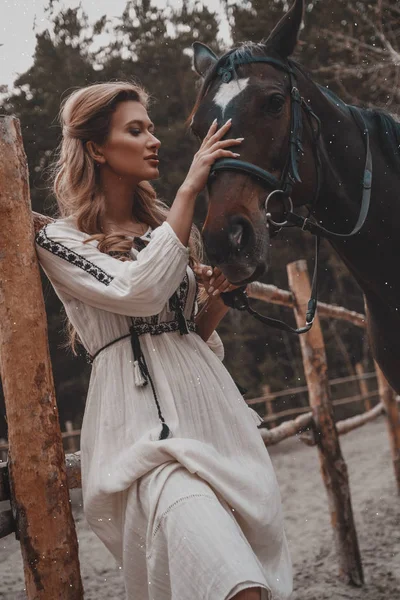 ドレスを着て美しく 柔らかい若い女性は 牧場で馬を抱きしめ なでています 魅力的なライダーは サドルの近くで屋外でポーズをとっています 自然景観 田園地帯 — ストック写真
