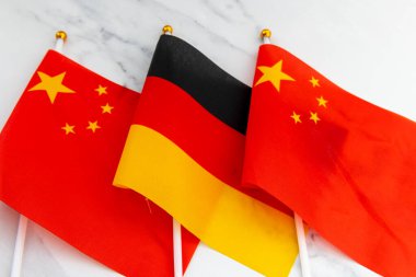 The national flag of Germany on flag pole in between the Chinese national flag. A Germany, China relations concept.