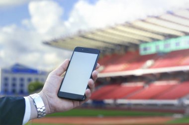 Dokunmatik ekran bir işadamı futbol stadyumu arka planı elinde bir cep telefonu. Fotoğraf için sahte.