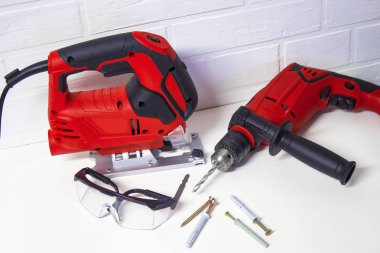 Bina için ahşap ve metal elektrik araçları profesyonel. Elektrik jig gördüm ve bir tuğla duvar arka plan üzerinde koruyucu gözlük ile matkap