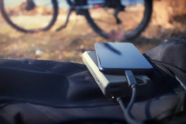Cargador portátil carga el teléfono inteligente. Banco de energía con cable sobre el fondo de la bicicleta — Foto de Stock
