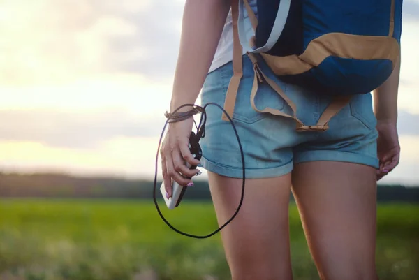 Sırt çantası olan bir kız. Turist elinde bir akıllı telefon ve orman ve gün batımı arka planda bir Power Bank tutar.