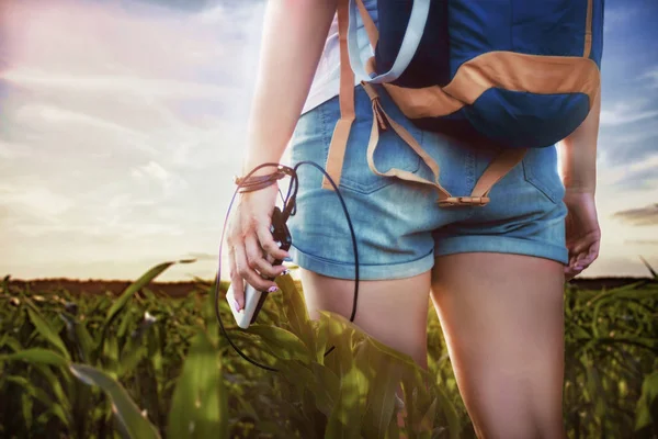 Ένα κορίτσι με σακίδιο σε ένα ταξίδι. Η τουριστική κρατά στο χέρι της ένα smartphone και μια τράπεζα ενέργειας στο φόντο του δάσους και του ηλιοβασιλέματος. — Φωτογραφία Αρχείου