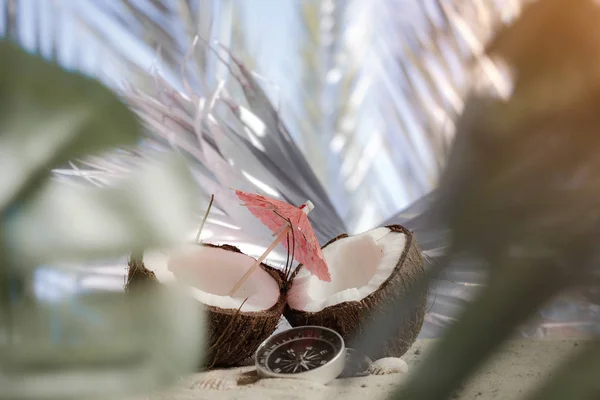 Hora de viajar. Duas metades de um coco com um guarda-chuva e uma bússola na praia contra o pano de fundo de uma folha de palmeira. Conceito sobre o tema do turismo . — Fotografia de Stock