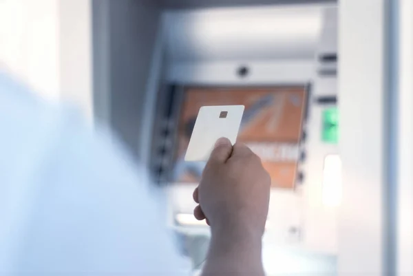 A man holds in his hand a mock-up of a white bank card near an ATM