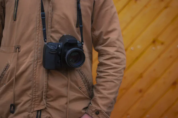 Un fotógrafo con una cámara alrededor del cuello sobre un fondo de madera . — Foto de Stock