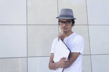 Gözlüklü ve şapkalı adam elinde belgeler tutuyor..