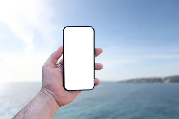 Adam elinde bir akıllı telefon tutuyor. Yakın plan, beyaz perdeli deniz manzaralı. Model Teknolojisi