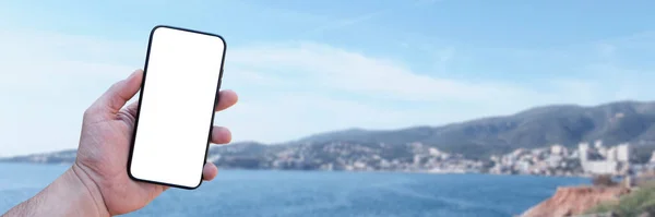 Time to travel. Smartphone in hand, against the background of the sea and the city under a sunny sky. Mock-up Technology