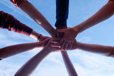 Bir grup insanın birleşmesi ve ekibin birliğinin gücü. Ortaklık ruhu konsepti. İnsanlar el ele tutuşur ve oğlanlar ve kızlar, gökyüzünde genç ve yetişkinler