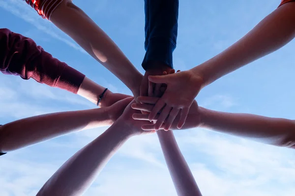 Unification in a group of people and the power of unity of the team. Partnership spirit concept. People hold hands together and boys and girls, adults and young on the sky background