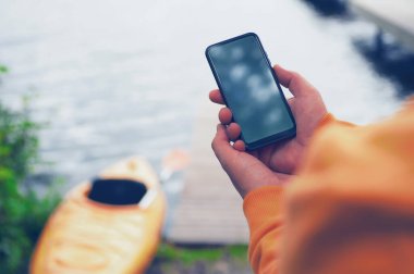Adamın elinde akıllı telefonu olan taşınabilir bir şarj aleti var. Suyun arka planında bir adam ve bir kano telefonu Güç Bankası 'yla şarj ediyor. Turizm konsepti