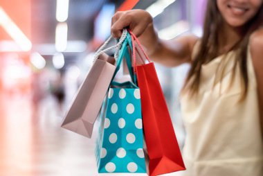 Elbiseli genç bir kadın elinde güzel ve parlak hediye çantalarıyla süpermarkette yürüyor.