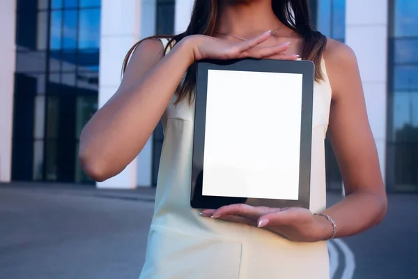 Young woman demonstrates the screen white screen tablet close-up. Mock up on the background of a modern business center